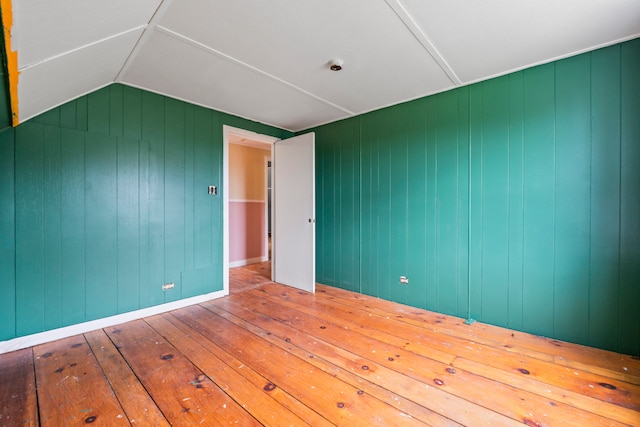 unfurnished room with hardwood / wood-style flooring, lofted ceiling, and wood walls