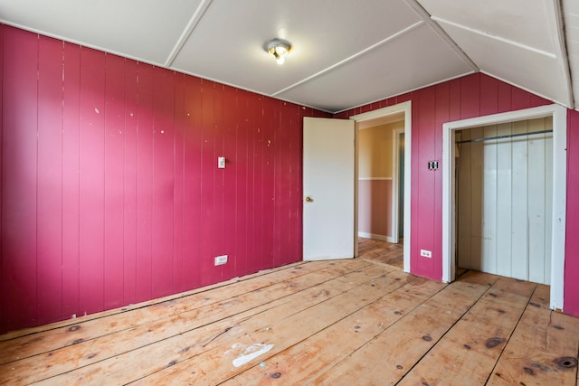 unfurnished bedroom featuring wooden walls, light wood-type flooring, and lofted ceiling