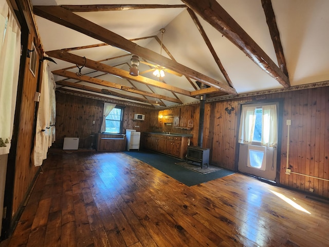 unfurnished living room featuring ceiling fan, vaulted ceiling with beams, a wood stove, wooden walls, and dark hardwood / wood-style floors