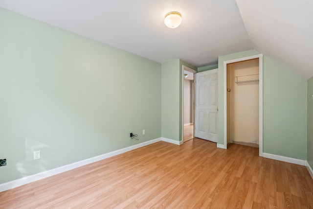 unfurnished bedroom featuring light wood-type flooring, a closet, and lofted ceiling