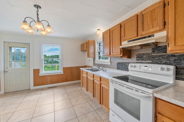 kitchen featuring white electric range oven, sink, decorative light fixtures, wooden walls, and an inviting chandelier