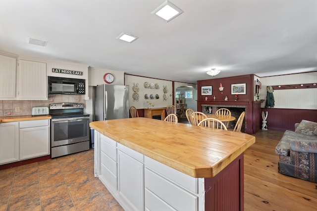 kitchen featuring wood-type flooring, white cabinets, a kitchen island, backsplash, and appliances with stainless steel finishes