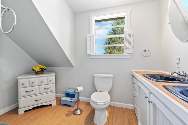 bathroom featuring wood-type flooring, lofted ceiling, vanity, and toilet