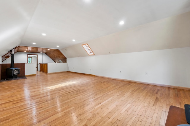 bonus room featuring a wood stove, vaulted ceiling with skylight, and light hardwood / wood-style floors