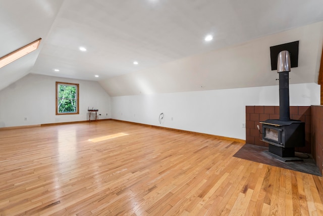 additional living space with light hardwood / wood-style flooring, a wood stove, and lofted ceiling