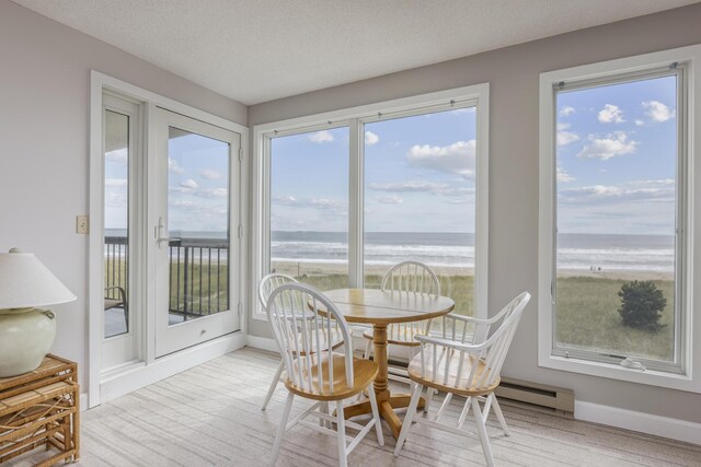 sunroom with a view of the beach, a baseboard heating unit, and a water view