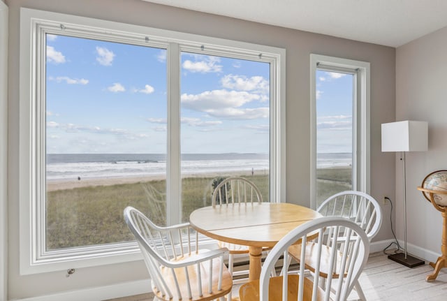 dining area featuring wood-type flooring, a water view, and a beach view