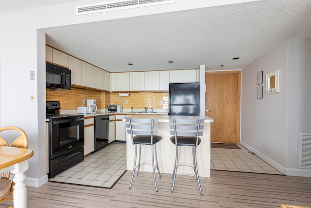 kitchen featuring a kitchen breakfast bar, tasteful backsplash, white cabinets, a kitchen island, and black appliances