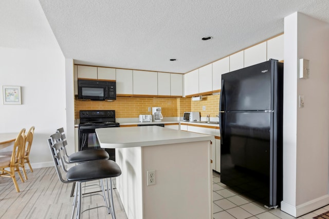 kitchen with decorative backsplash, white cabinets, black appliances, and a center island