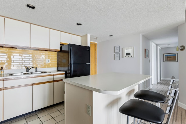 kitchen with black fridge, sink, white cabinetry, a center island, and a breakfast bar area