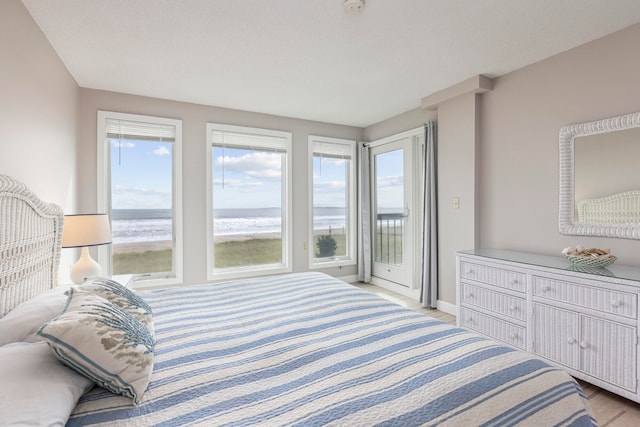 bedroom with access to outside, light hardwood / wood-style flooring, and a water view