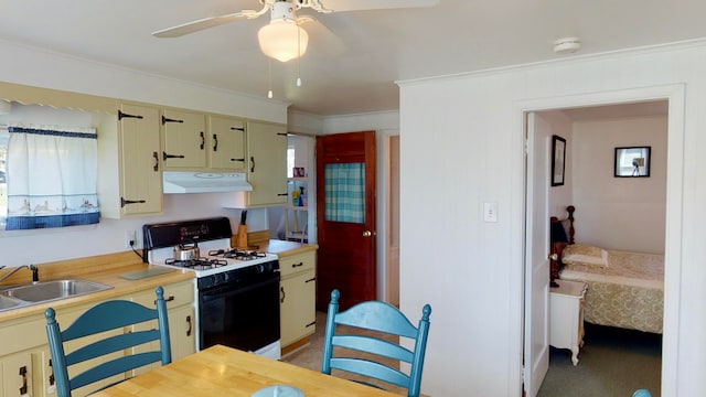 kitchen featuring sink, gas range, crown molding, ceiling fan, and cream cabinetry