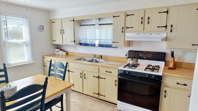 kitchen with sink, ventilation hood, cream cabinets, and range with gas cooktop