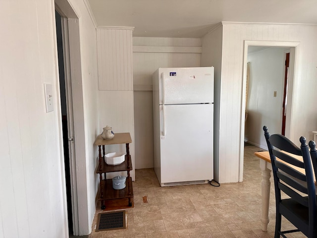 kitchen with crown molding, wooden walls, and white refrigerator