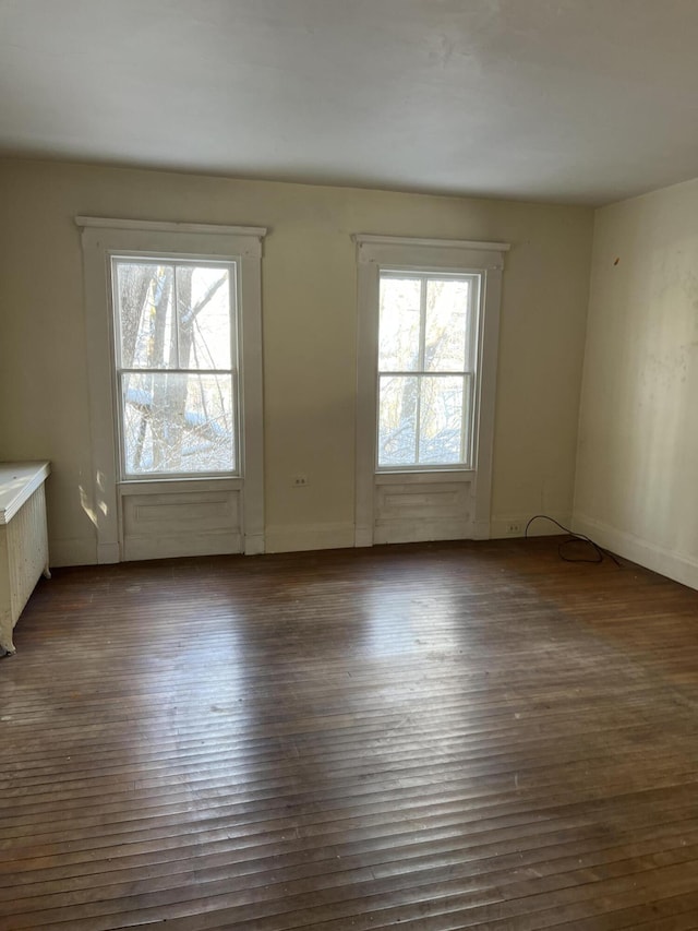 unfurnished room featuring a healthy amount of sunlight, dark hardwood / wood-style floors, and radiator heating unit