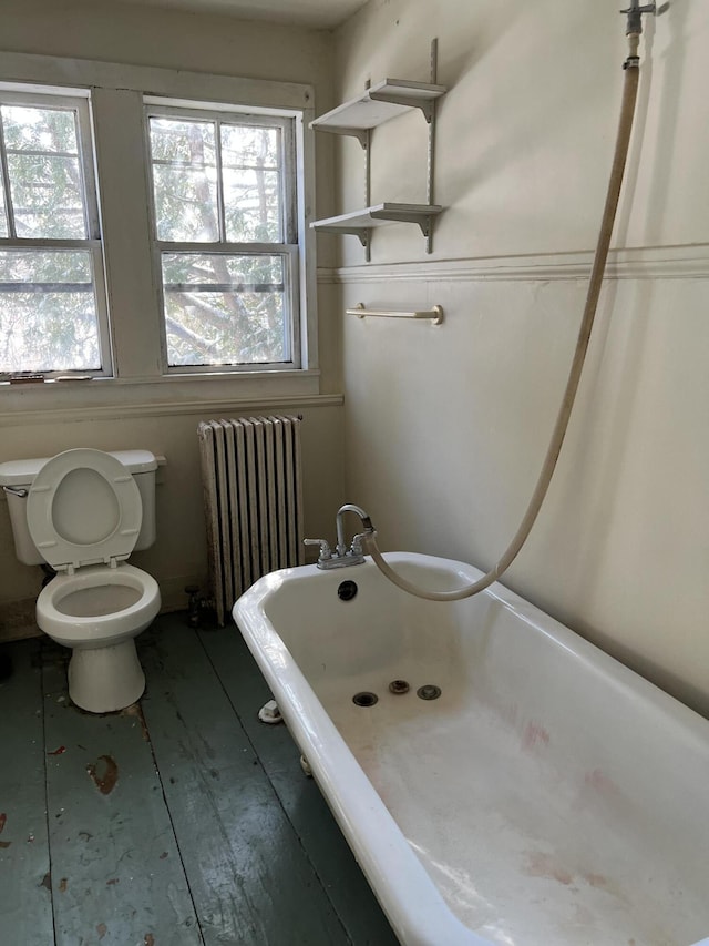 bathroom featuring radiator, hardwood / wood-style flooring, toilet, and a tub to relax in