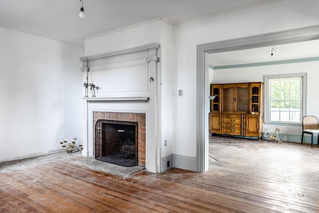unfurnished living room with baseboards, crown molding, wood-type flooring, and a brick fireplace