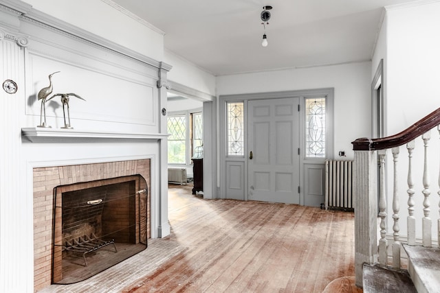 entryway featuring ornamental molding, radiator heating unit, light wood finished floors, and a brick fireplace