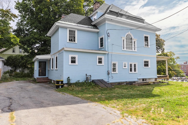 view of front facade with entry steps, a chimney, a front yard, and roof with shingles