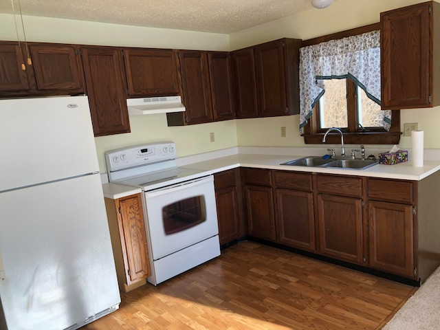 kitchen with a textured ceiling, wood-type flooring, white appliances, and sink