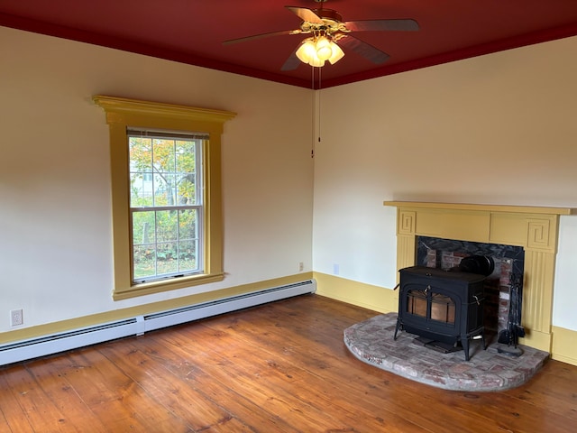 unfurnished living room featuring a wood stove, ceiling fan, ornamental molding, hardwood / wood-style floors, and a baseboard heating unit