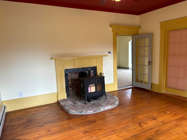 living room featuring wood-type flooring, a baseboard radiator, a wood stove, and ceiling fan