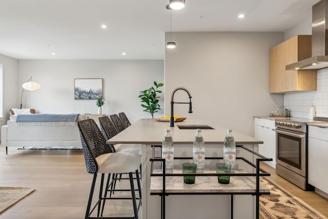 kitchen with backsplash, light wood finished floors, a kitchen bar, stainless steel electric range, and wall chimney range hood