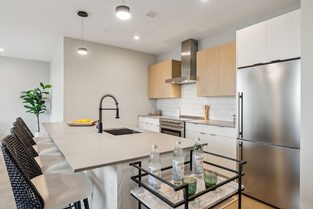 kitchen with hanging light fixtures, sink, wall chimney exhaust hood, white cabinetry, and stainless steel appliances