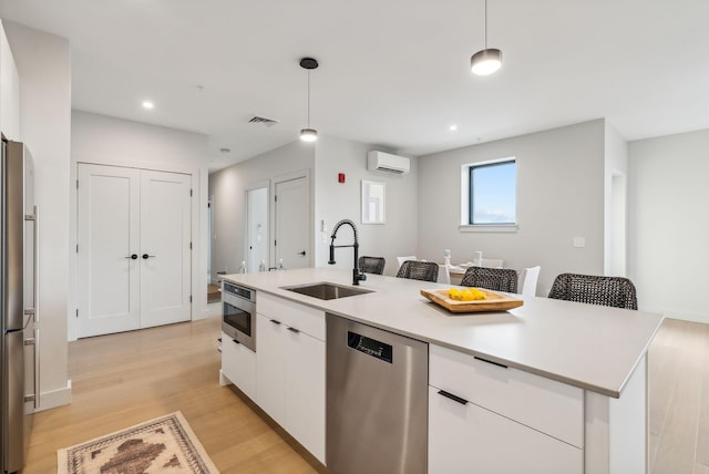 kitchen with pendant lighting, sink, a center island with sink, white cabinetry, and appliances with stainless steel finishes