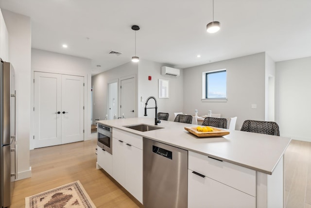kitchen with white cabinets, stainless steel appliances, a sink, light wood-type flooring, and an AC wall unit