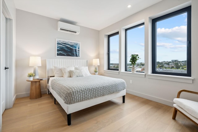 bedroom with light hardwood / wood-style flooring, multiple windows, and an AC wall unit