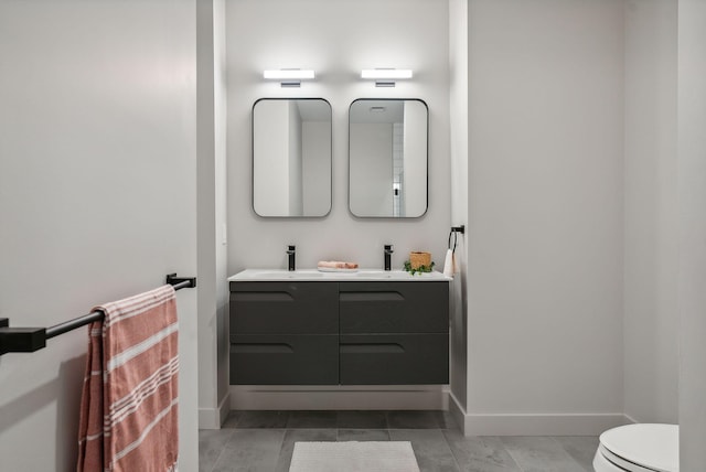 bathroom featuring baseboards, toilet, double vanity, and a sink
