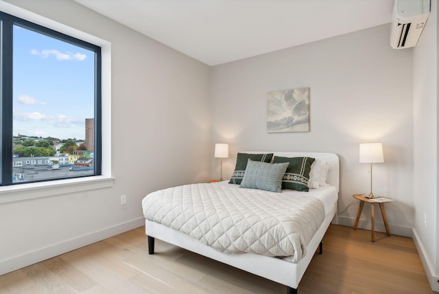 bedroom featuring multiple windows, wood finished floors, a wall mounted air conditioner, and baseboards
