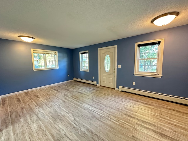 entryway with a textured ceiling, light wood-type flooring, baseboard heating, and a wealth of natural light