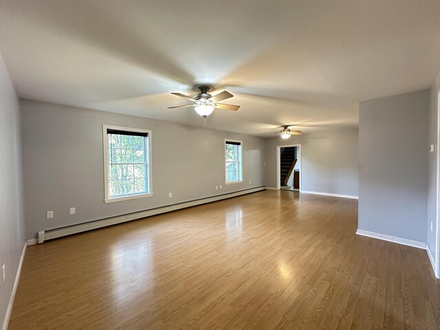 unfurnished living room with a baseboard radiator, hardwood / wood-style floors, ceiling fan, and a wealth of natural light