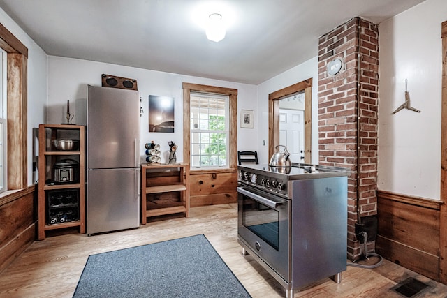 kitchen with wood walls, light hardwood / wood-style floors, and appliances with stainless steel finishes