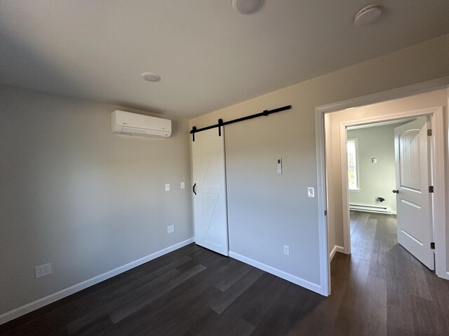 unfurnished bedroom with a barn door, dark hardwood / wood-style flooring, a baseboard heating unit, and a wall unit AC