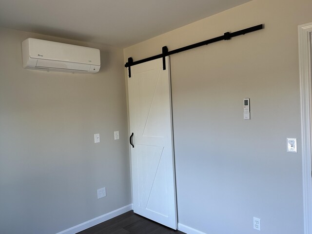 unfurnished bedroom featuring dark hardwood / wood-style flooring, a barn door, and a wall mounted AC