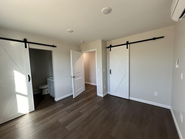 unfurnished bedroom featuring an AC wall unit, connected bathroom, dark wood-type flooring, and a barn door