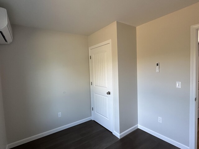 unfurnished bedroom with an AC wall unit and dark wood-type flooring