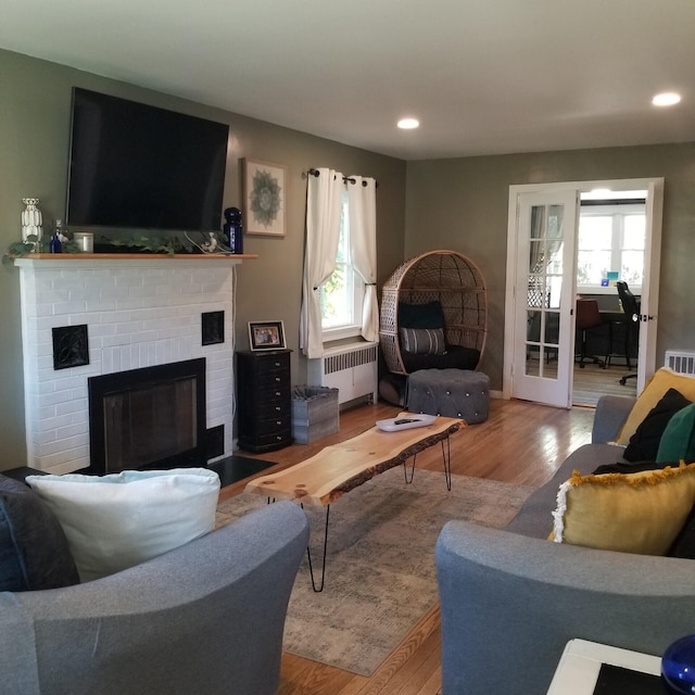 living room with a brick fireplace, radiator, hardwood / wood-style flooring, and a healthy amount of sunlight