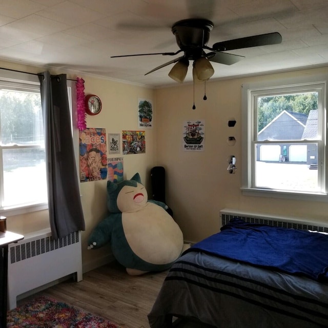 bedroom featuring wood-type flooring, ornamental molding, ceiling fan, and radiator heating unit