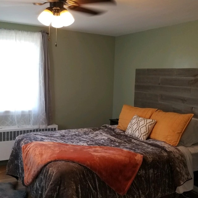 bedroom featuring radiator heating unit, ceiling fan, and multiple windows