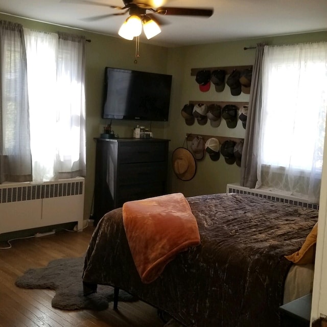 bedroom with multiple windows, wood-type flooring, ceiling fan, and radiator heating unit