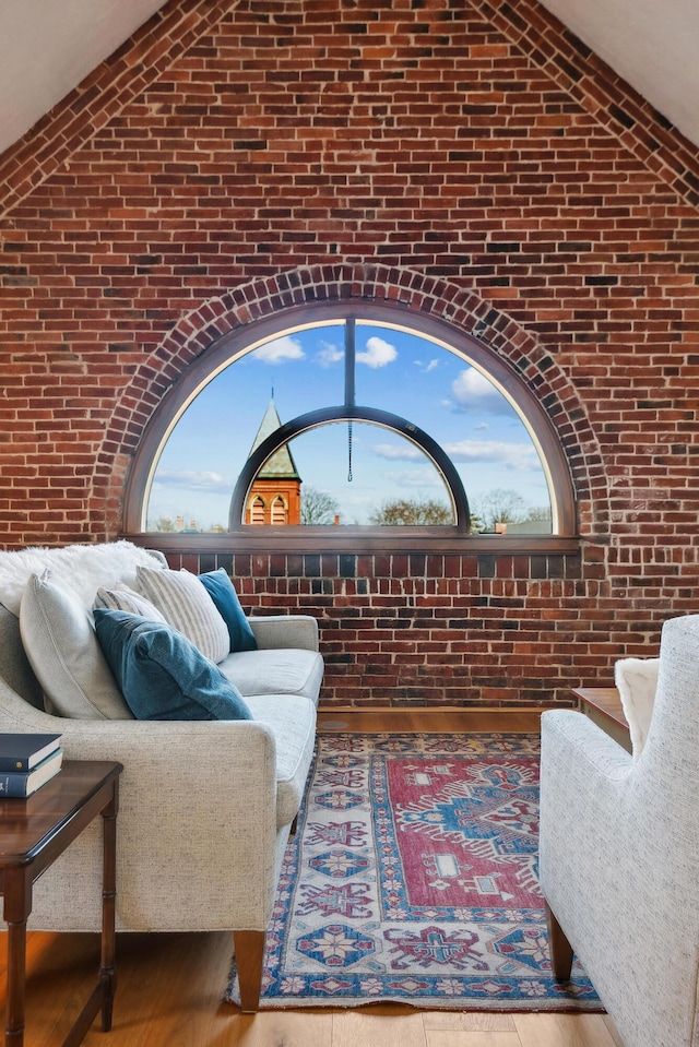 living area featuring vaulted ceiling, wood finished floors, and brick wall