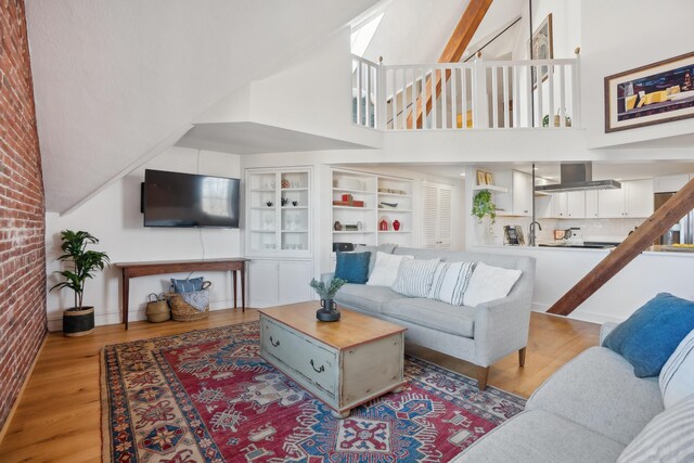 living room with high vaulted ceiling, wood finished floors, a skylight, and brick wall