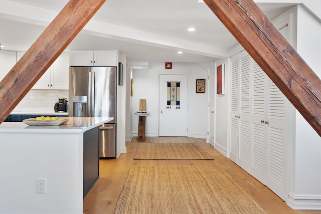 kitchen featuring light countertops, stainless steel fridge, decorative backsplash, beam ceiling, and light wood-style flooring
