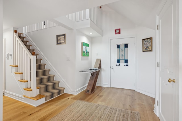 entryway with vaulted ceiling, baseboards, light wood-style floors, and stairway