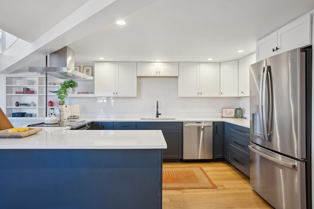 kitchen featuring light countertops, a sink, open shelves, wall chimney exhaust hood, and stainless steel appliances
