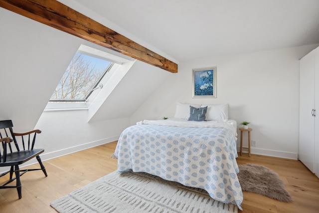 bedroom featuring vaulted ceiling with skylight, baseboards, and wood finished floors